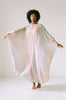 Woman standing in center of white room wearing a flowy, hand dyed 1970's Halston Kaftan