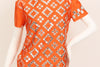 Orange, short-sleeve, mock-neck shirt with a silver, graphic print with mirrored embellishments. 
