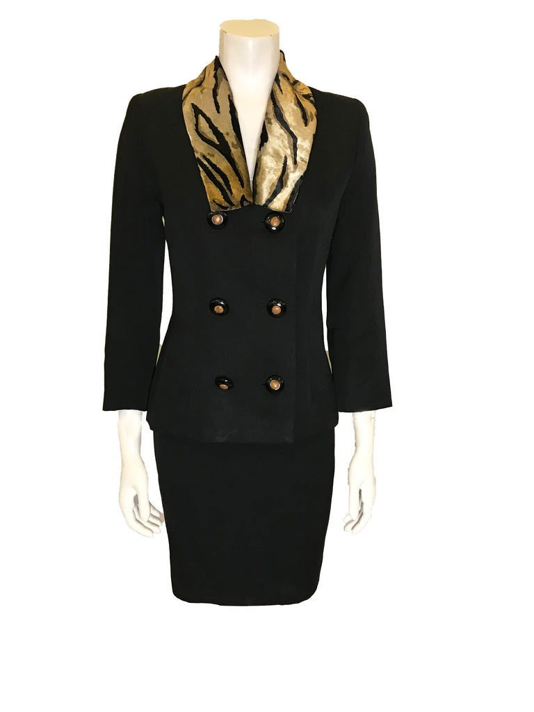 black two-piece suit with skirt. Jacket has faux fur, animal-print collar and double-breasted, pearlized buttons. Skirt is straight and knee-length.