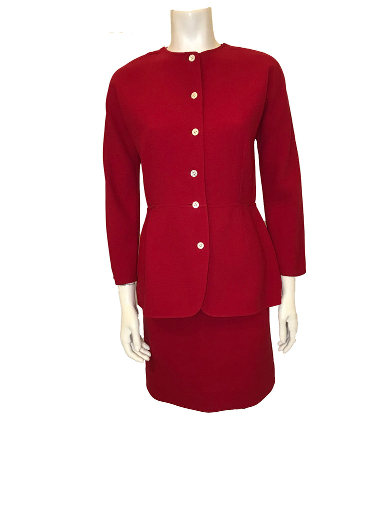 Red, two-piece skirt-suit. Jacket is hip length and has three quarter sleeves and pearlescent buttons. The skirt is straight and knee length.