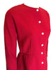 Red, two-piece skirt-suit. Jacket is hip length and has three quarter sleeves and pearlescent buttons. The skirt is straight and knee length.