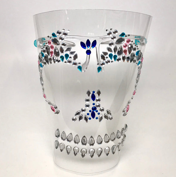 Clear plastic shield with a rhinestone skull motif in multicolored rhinestones. Shield is worn on face by two arms that rest on ears. 