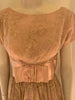 Closeup of the neckline of a light pink 1950s dress with short sleeves and a large bow at the waist