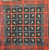 Emanuel Ungaro scarf with a black background and oversize windowpane plaid motif in coral and grey-blue. In the squares of the plaid, there are small clusters of blue and white flowers.