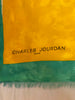 Close up of designer's name "Charles Jourdan" on lower lefthand corner of a silk scarf. The background is sea foam green and marigold colored.