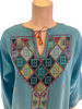 Closeup front view of the neckline of an aqua blue kaftan showing embroidery in shades of red, white, green, yellow, orange, and blue