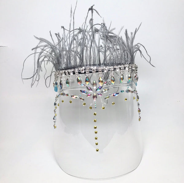 Clear face shield with rhinestones and crystals  with a grey feather trim on top Shield is worn on face with 2 arms that rest on the ears. 