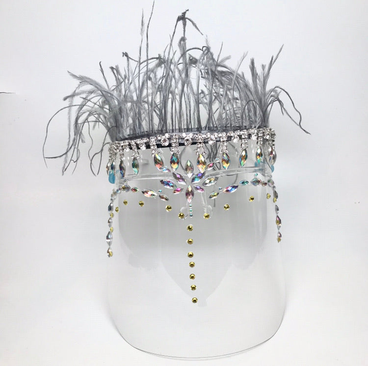 Clear face shield with rhinestones and crystals  with a grey feather trim on top Shield is worn on face with 2 arms that rest on the ears. 