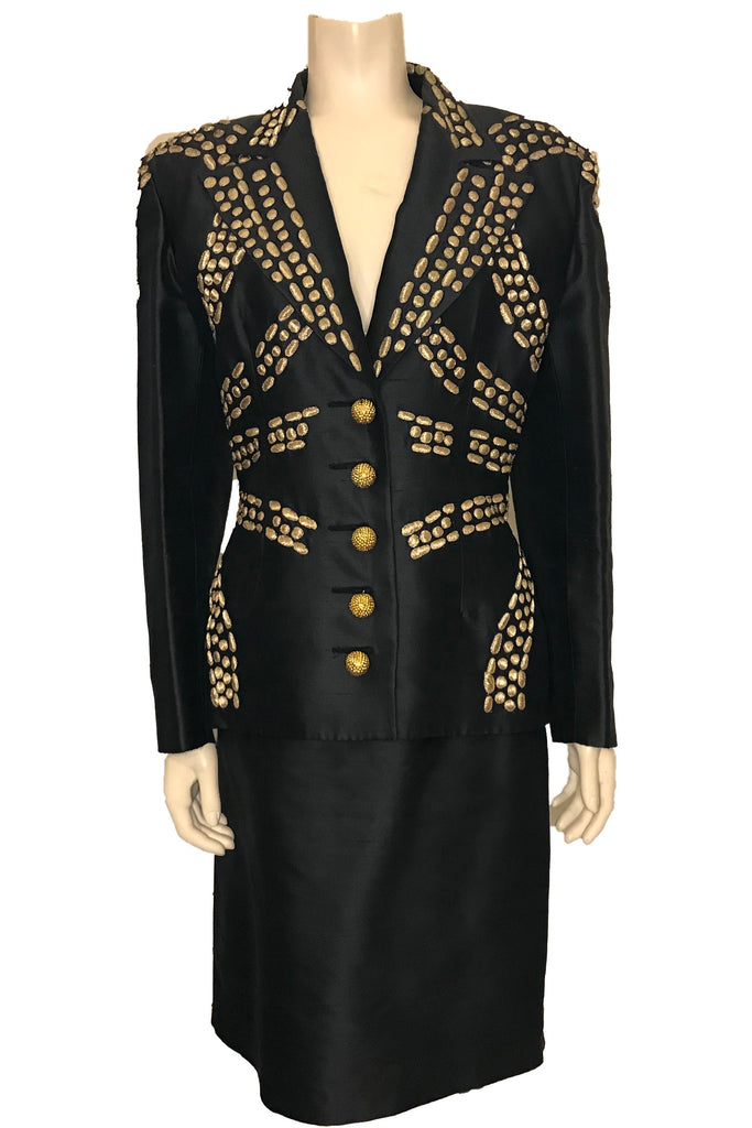 Navy blue suit with straight knee length skirt. Jacket is embellished with gold metallic thread across front. Jacket closure is five gold buttons.
