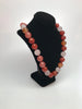 Diagonal side view of necklace display wearing a necklace of faceted round beads in varying shades of rose and orange