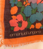 Closeup of designer's name "emanuel ungaro" on lower left hand corner of floral print scarf in shades of coral, periwinkle, blue, orange, and green.