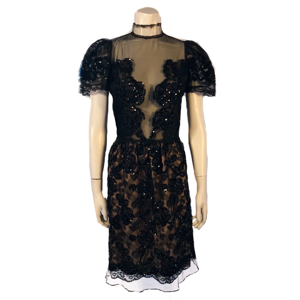 Short sleeve evening dress covered in lace and black beading. The front has a sheer insert. Skirt is knee length.